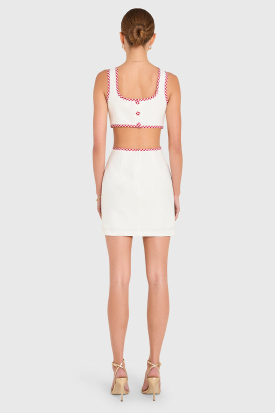 Amanda Uprichard | Beeba Dress in Ivory. Model wears a white mini dress with red gingham trim against a white backgorund. view 3