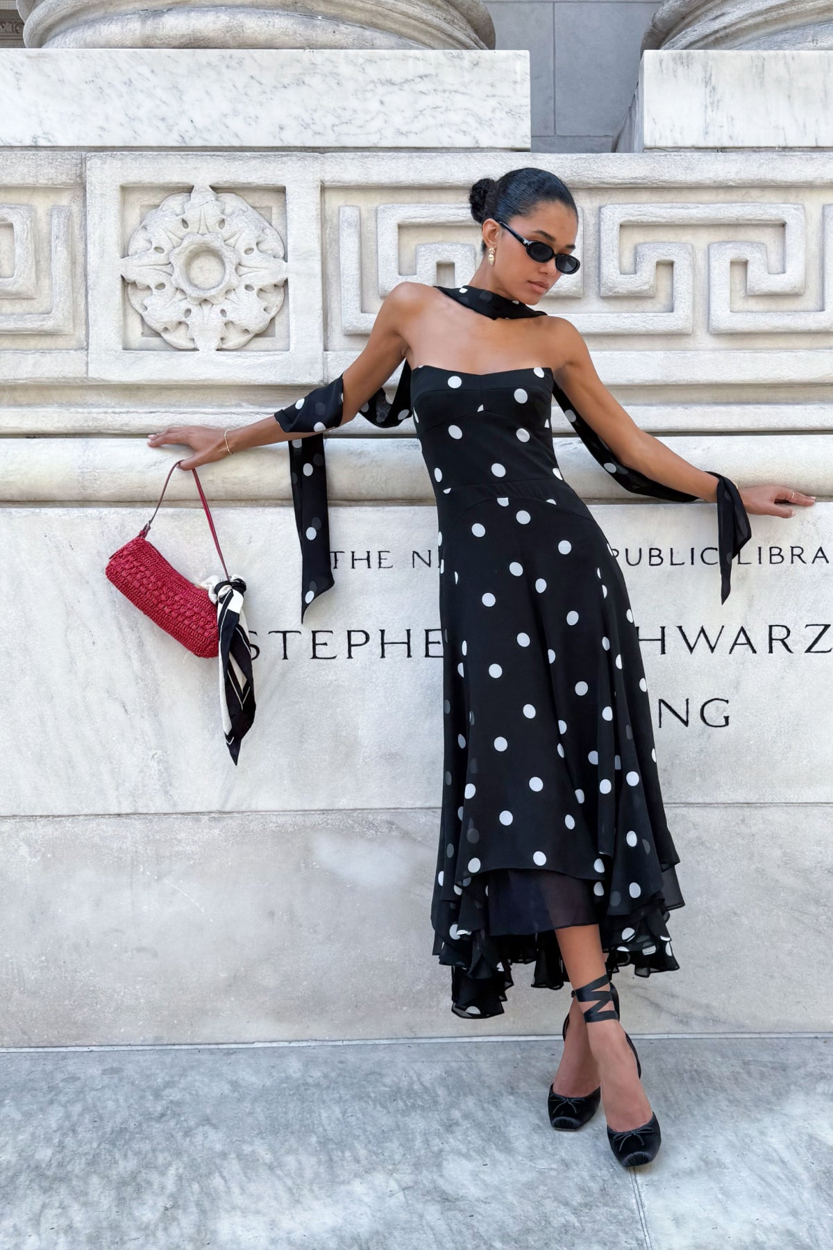 Woman in a black polka dot dress standing against a marble wall.