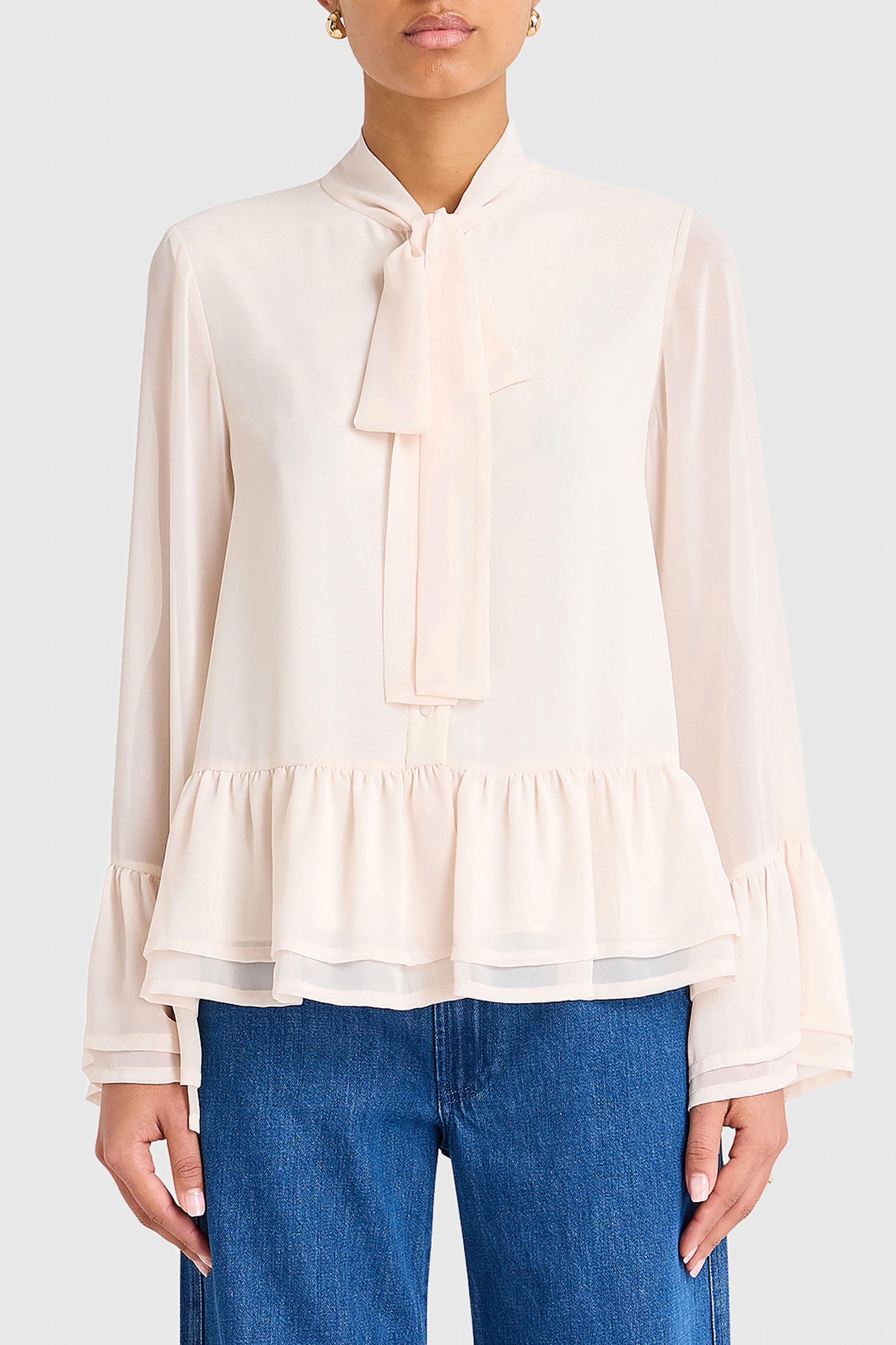Beige blouse with a bow detail worn by a person on a white background