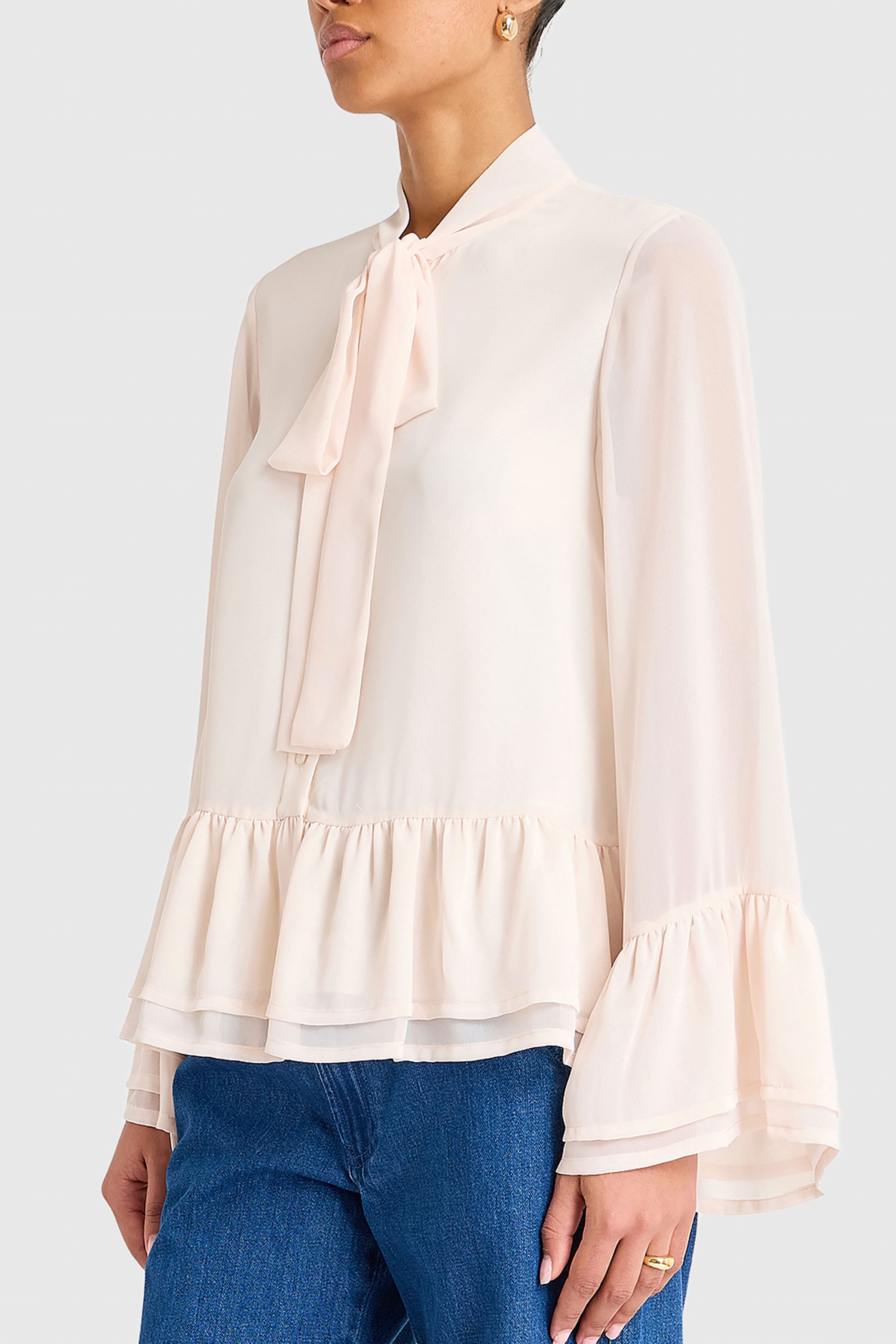 Woman wearing a light pink blouse with a bow tie and blue jeans on a white background