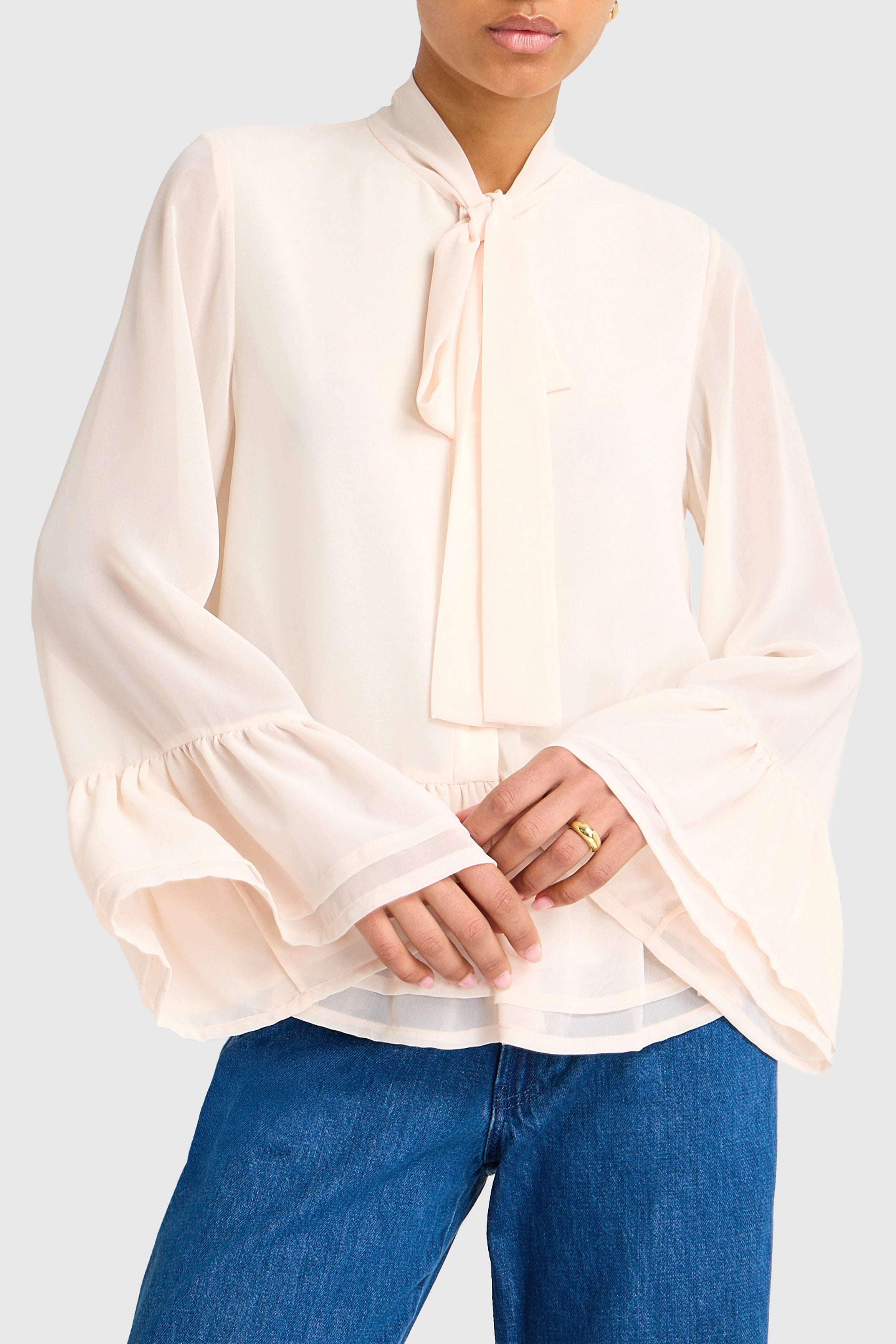 Person wearing a cream blouse with long sleeves and blue jeans on a light gray background