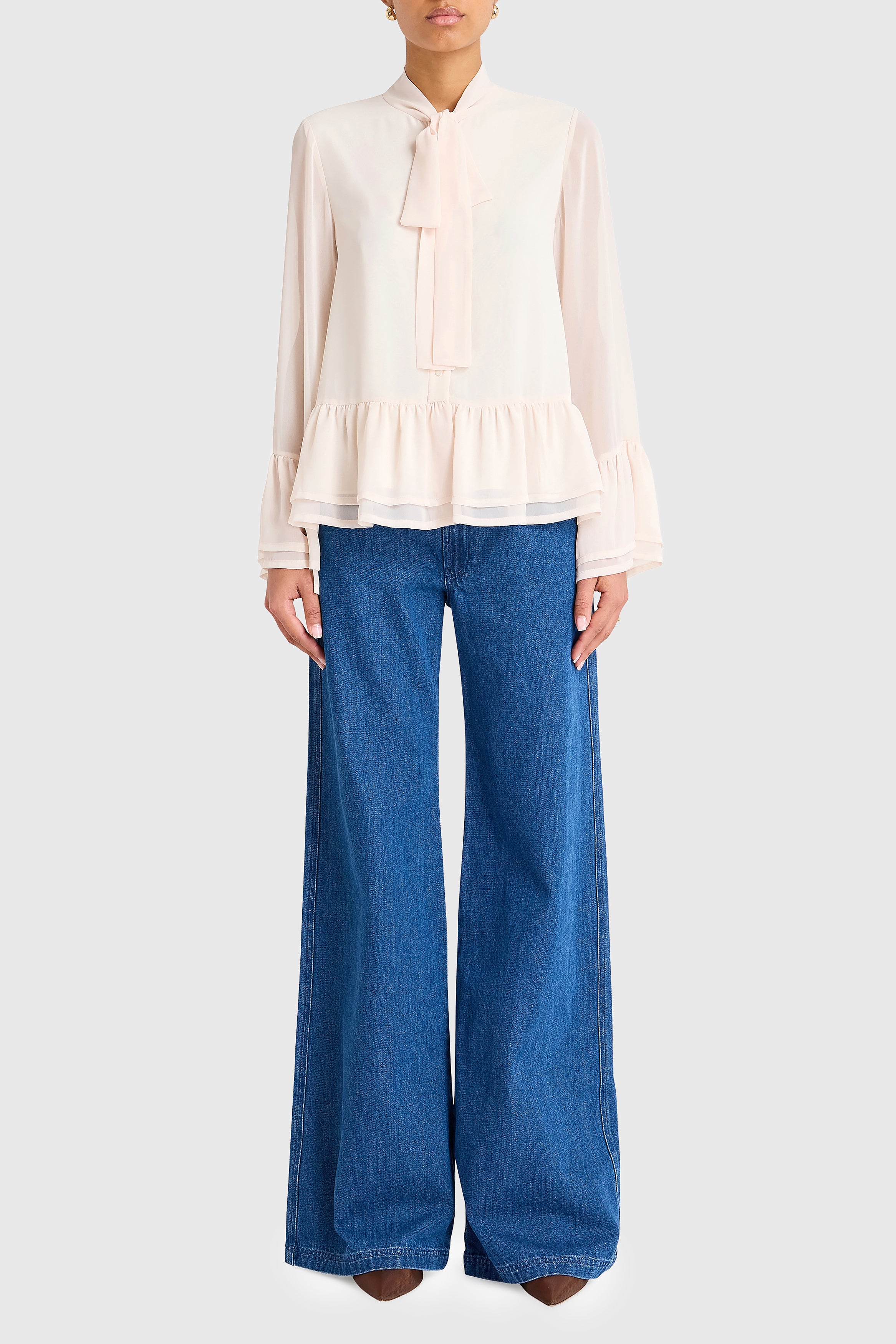 Person wearing a beige blouse and blue jeans on a white background