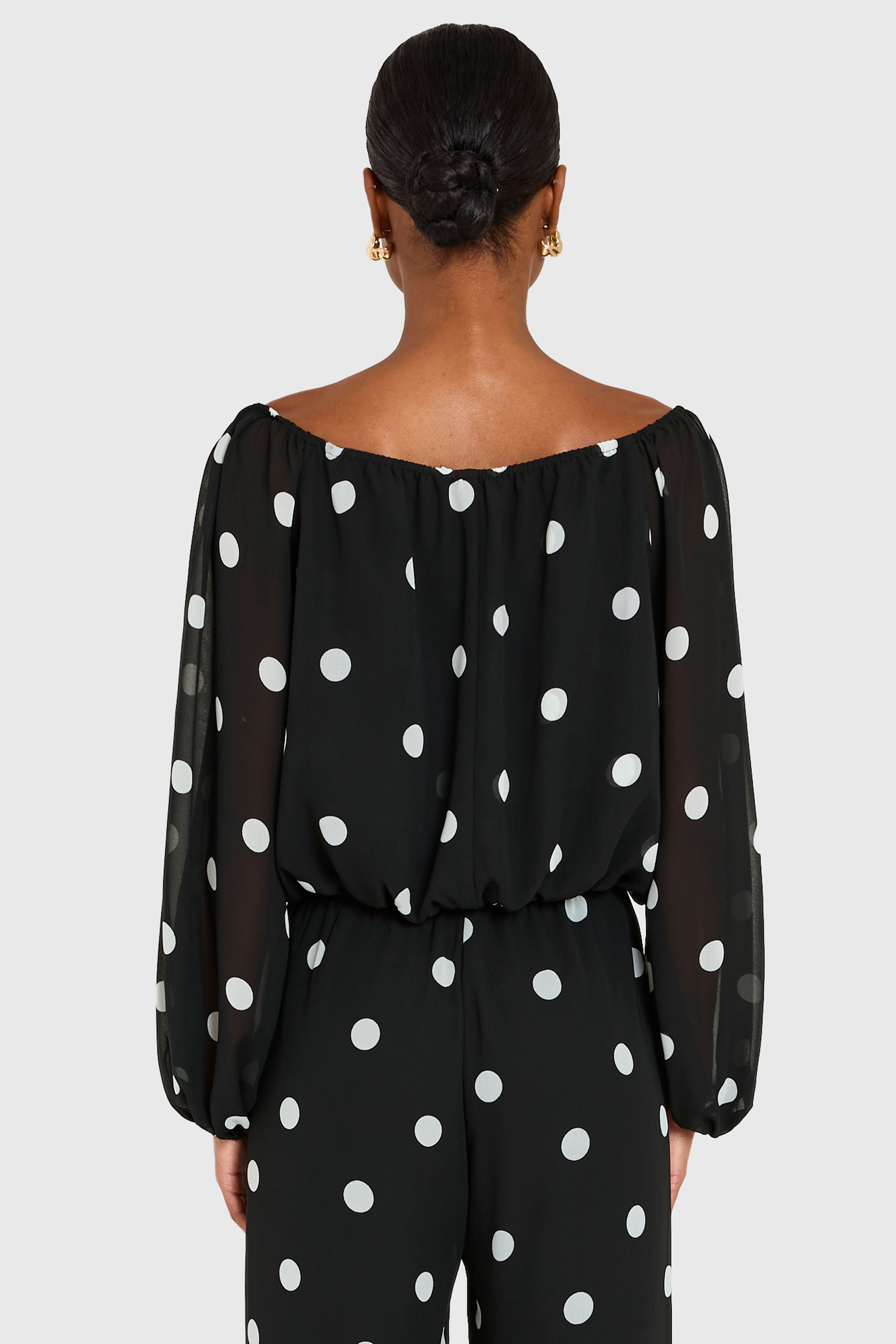 Black off-shoulder top with white polka dots worn by a model on a light gray background
