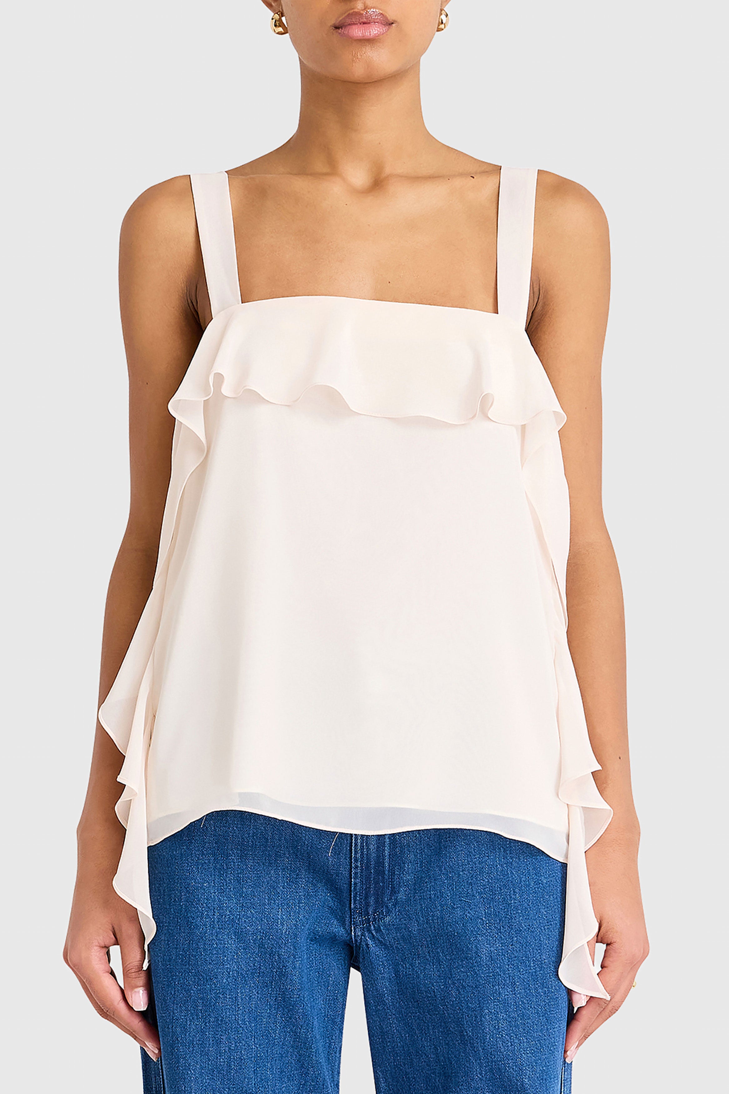 Woman wearing a white ruffled top and blue jeans on a plain background