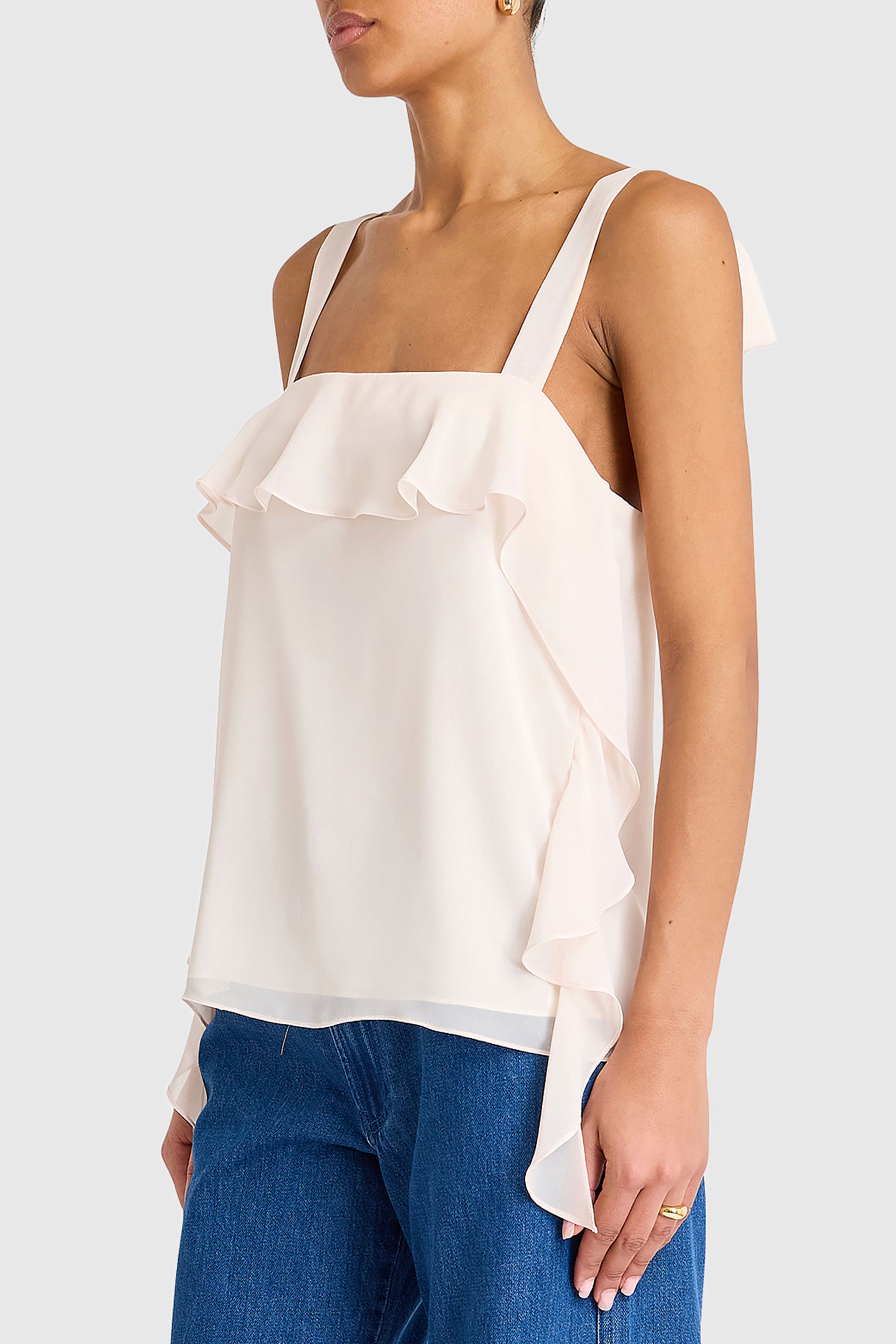 Woman wearing a white ruffled top and blue jeans on a plain background