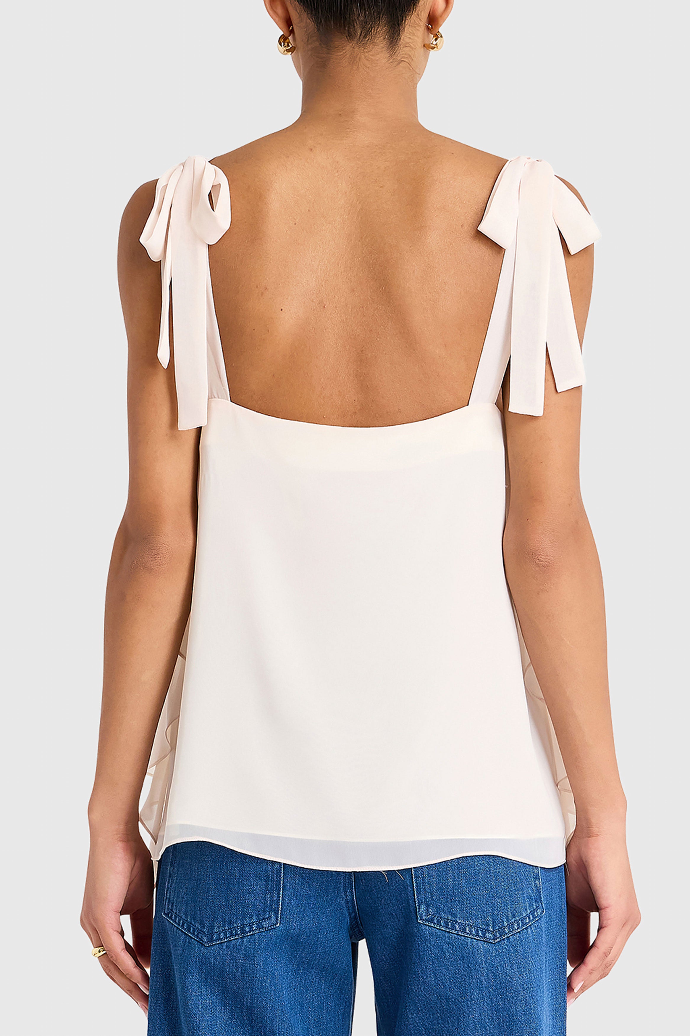 Woman wearing a white top with bow straps and blue jeans on a plain background