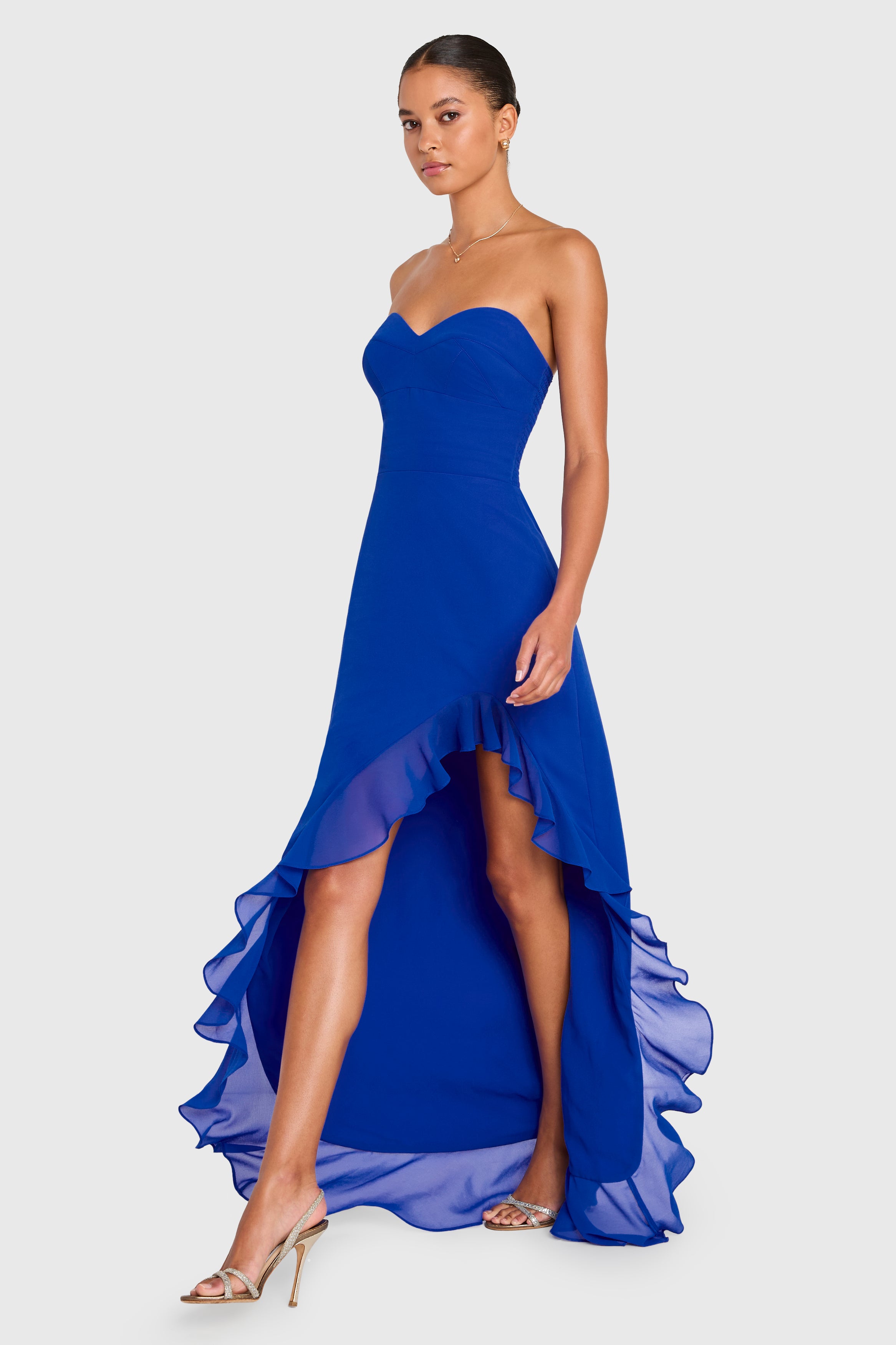 Woman wearing a strapless blue gown with a high-low hem on a white background