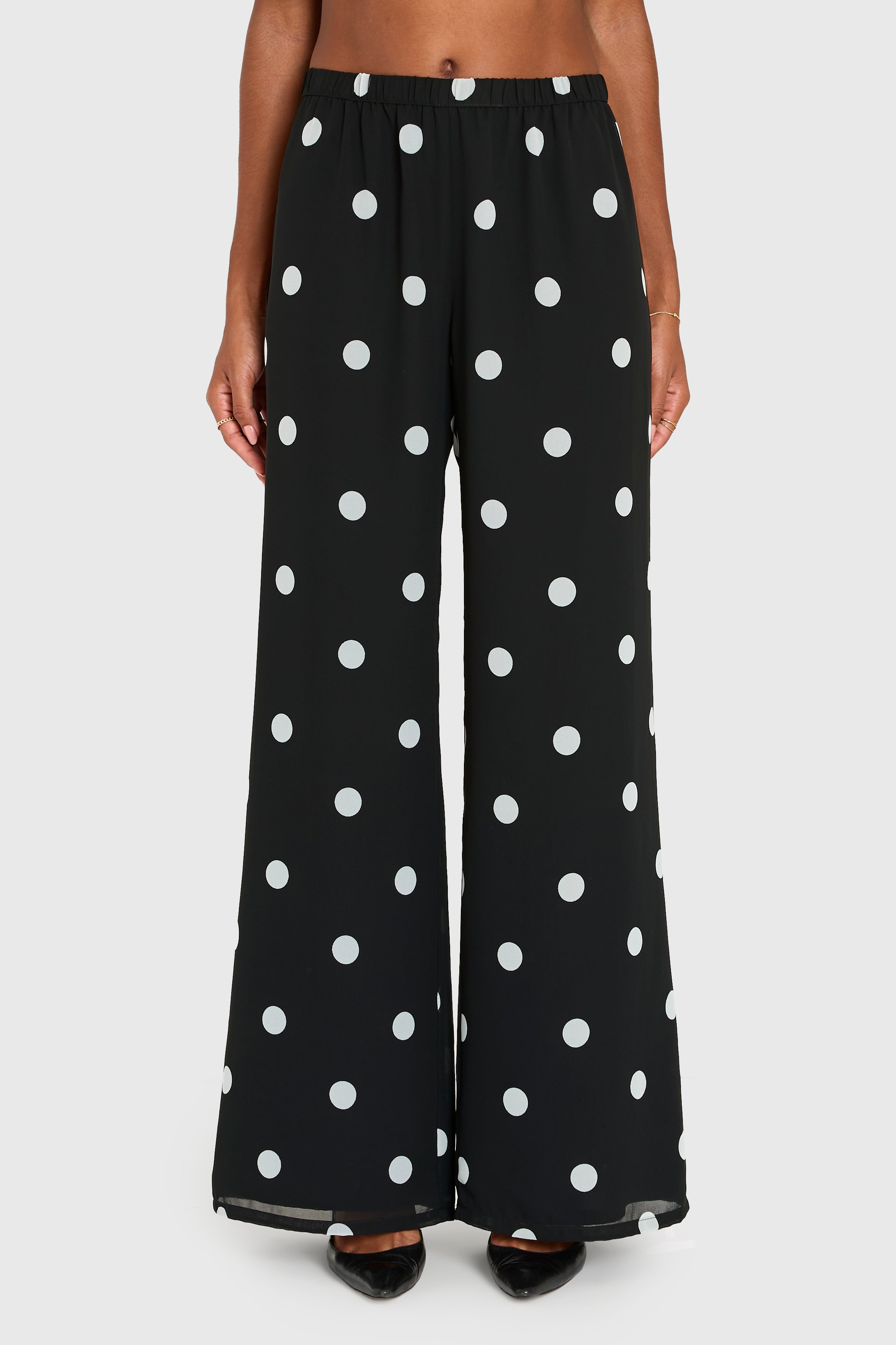 Black pants with white polka dots worn by a person on a white background
