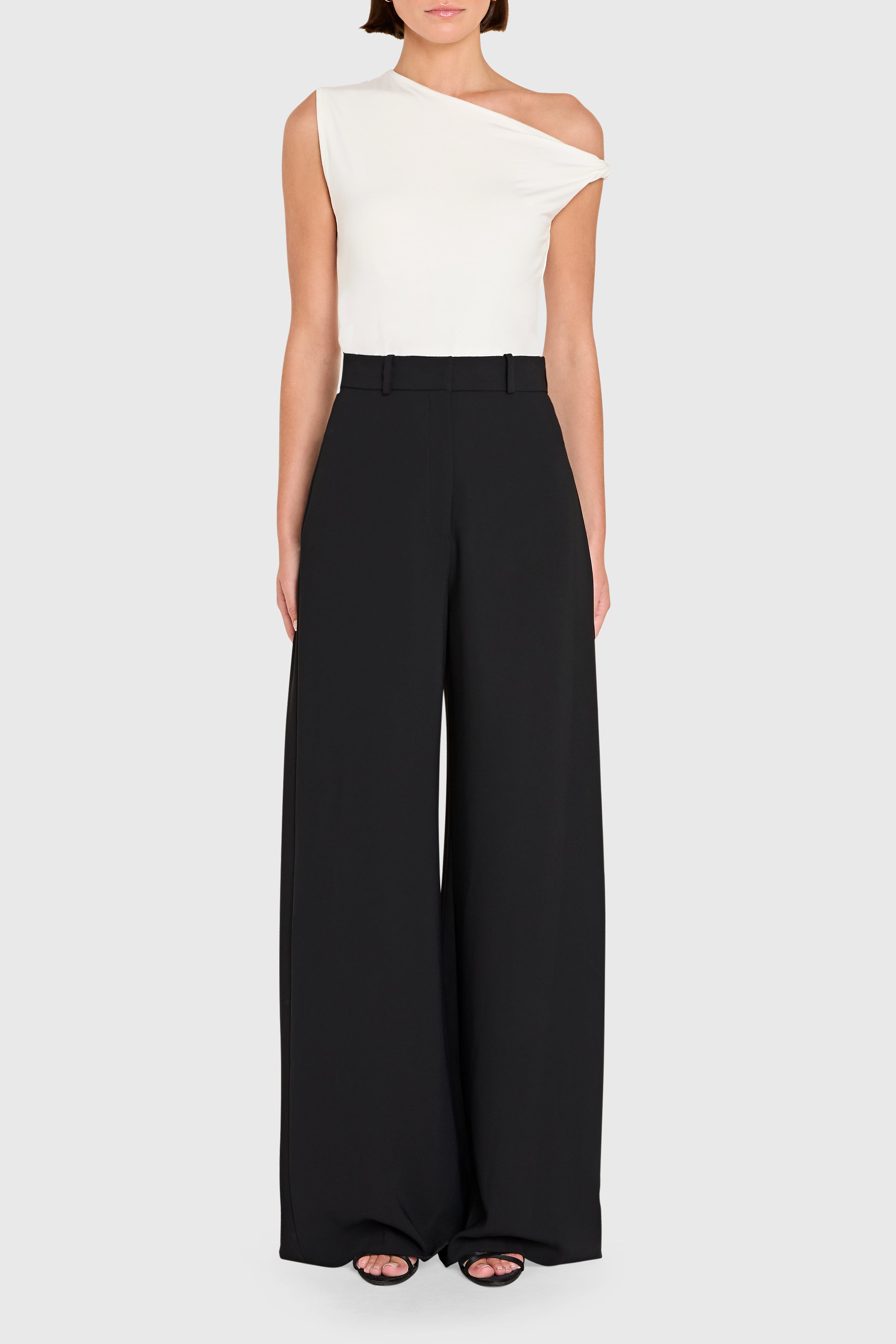 Woman wearing a white one-shoulder top and black wide-leg pants on a white background