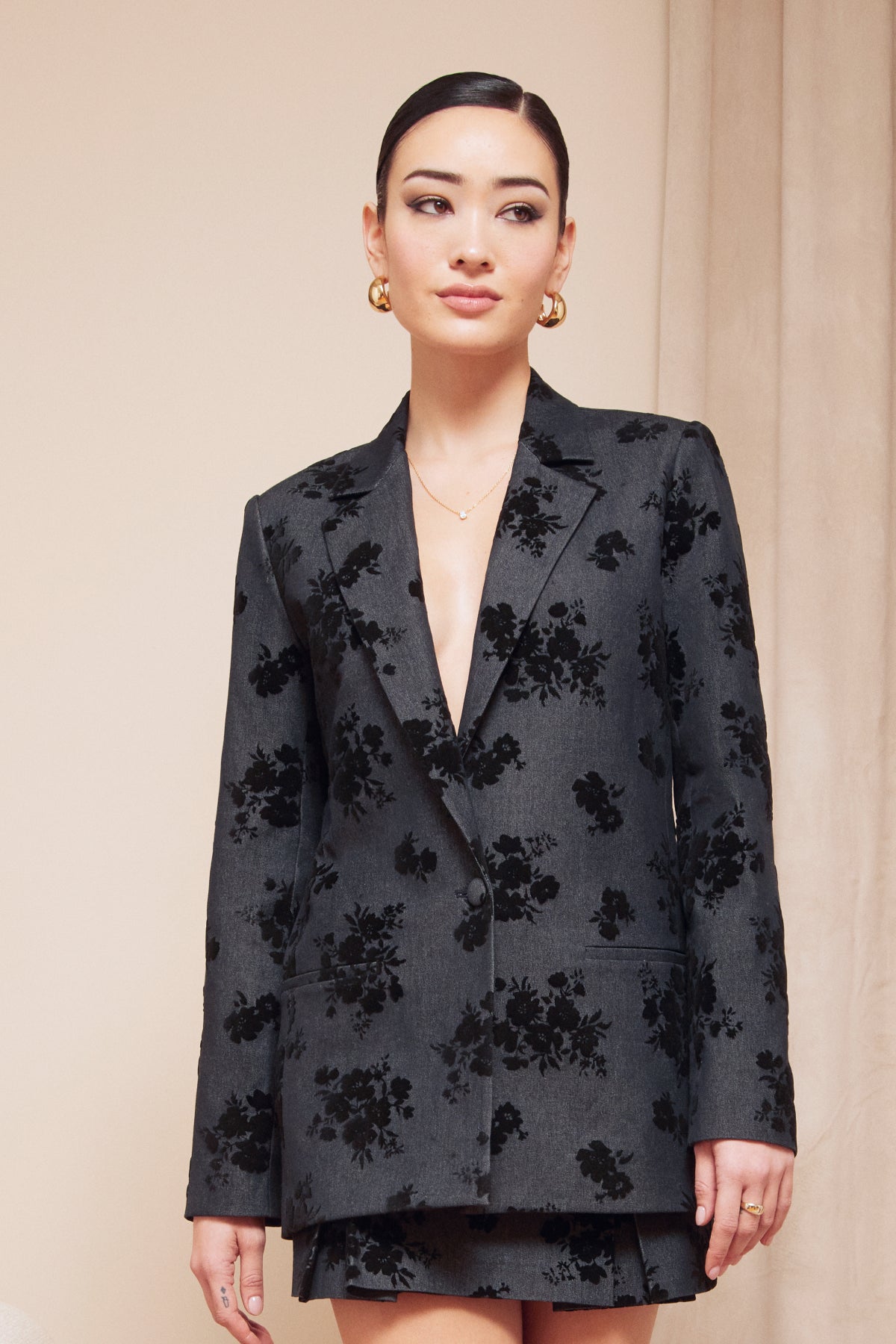 Woman wearing a black floral blazer against a beige background