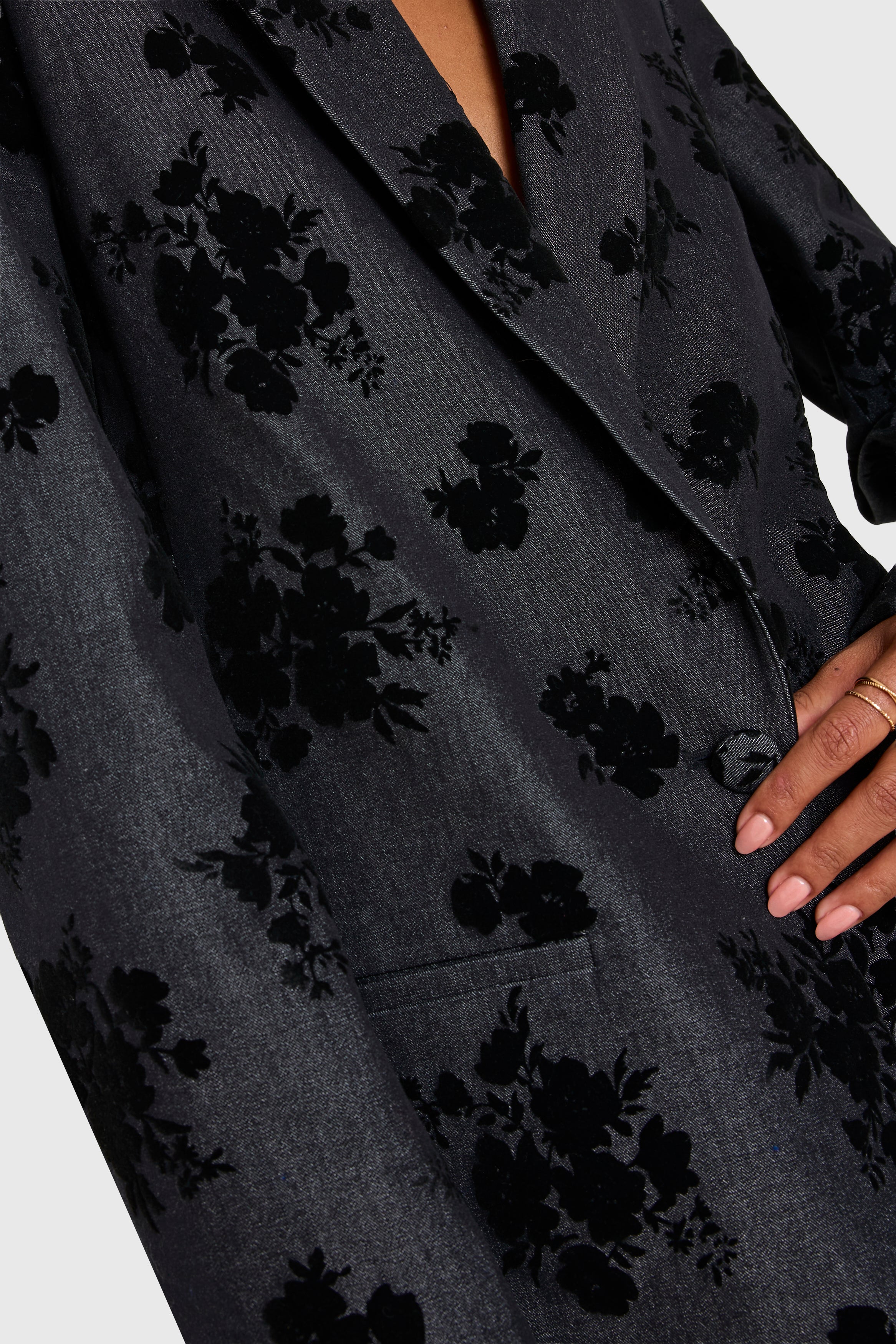 Dark floral patterned coat with a hand visible on a light gray background