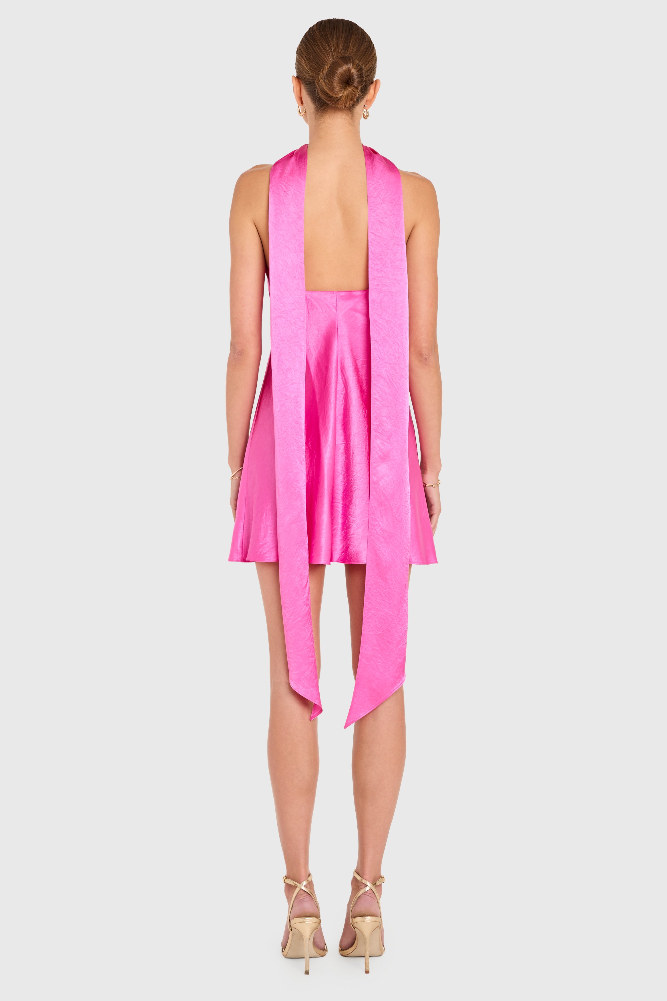 Woman wearing a pink dress with a halter neck design on a white background