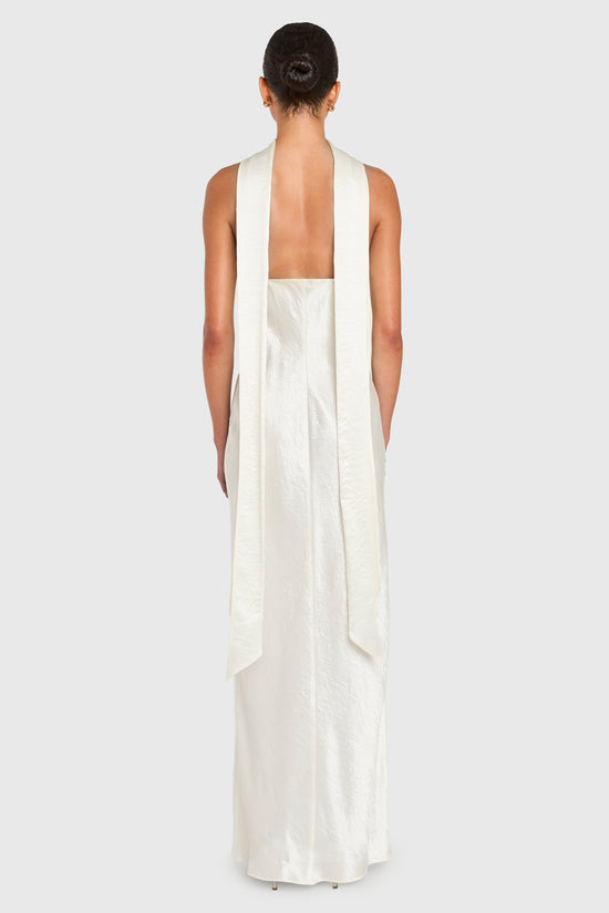 Woman wearing a long, white dress with a halter neck design on a plain background