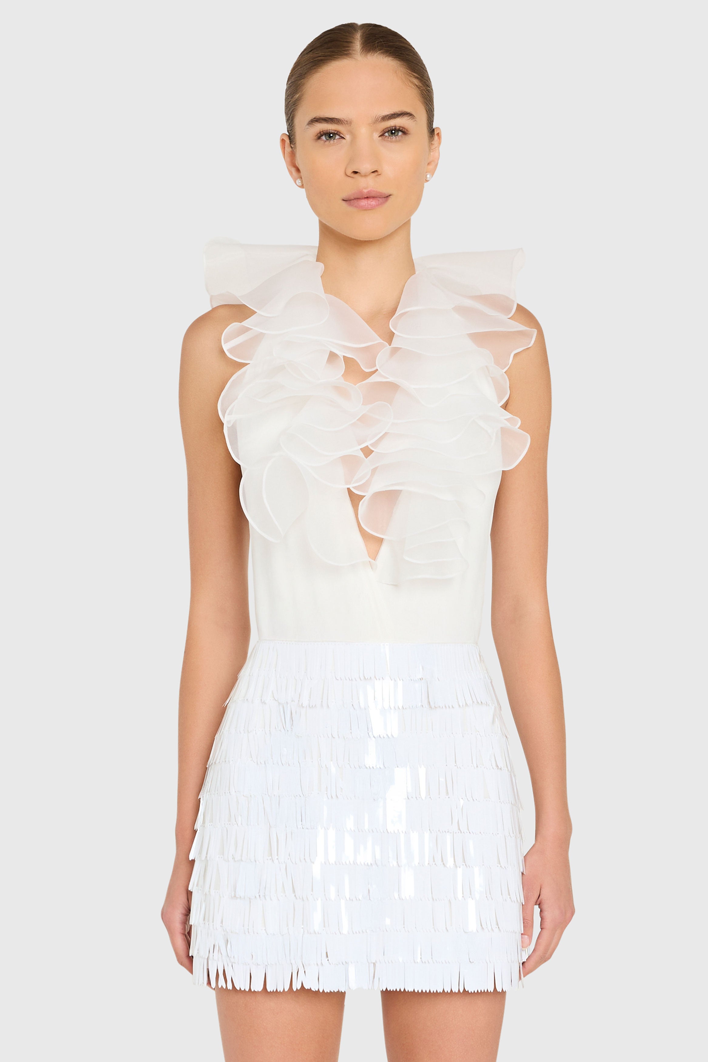 Woman wearing a white dress with ruffled top and fringe skirt on a plain background