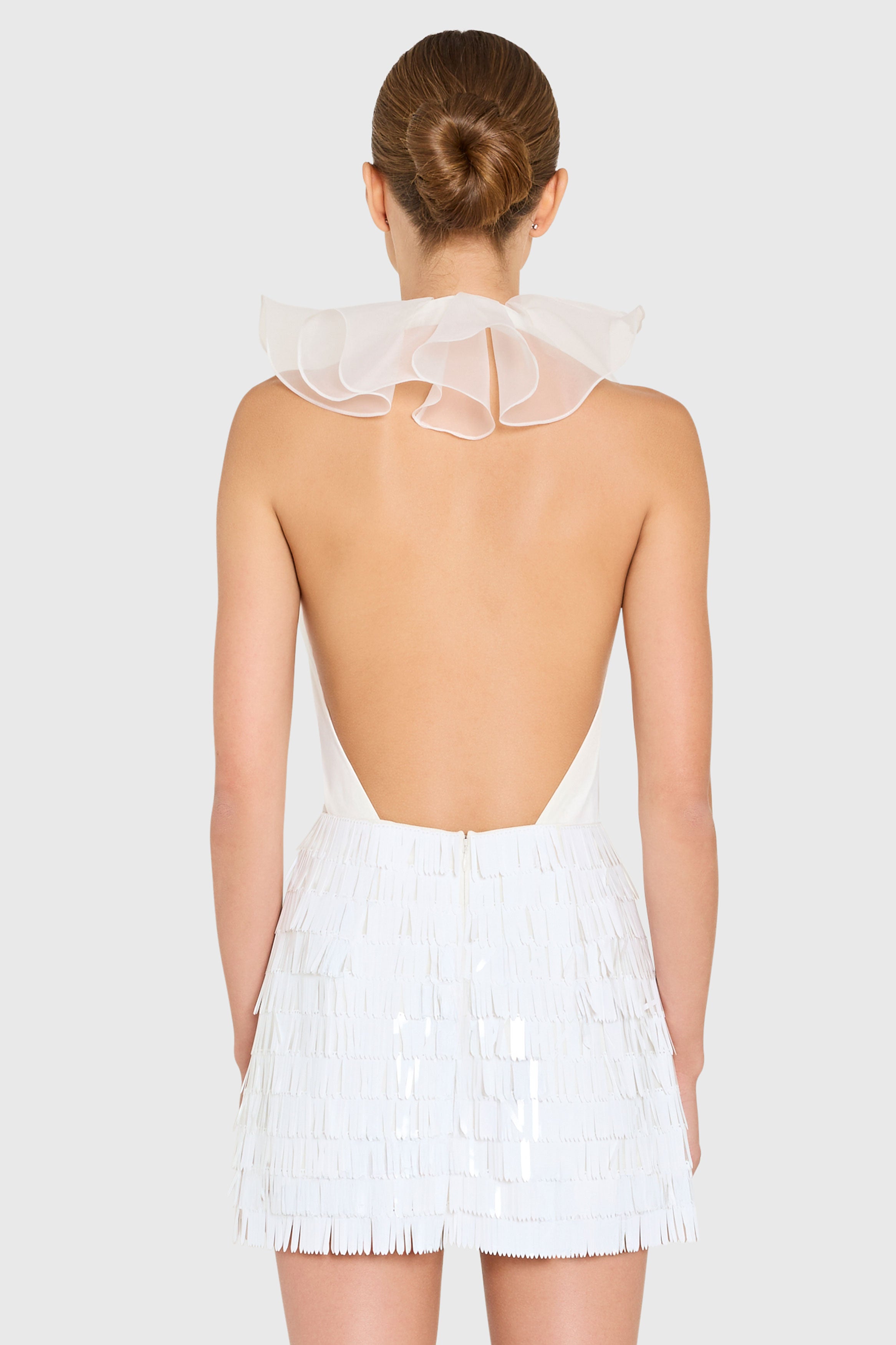 White dress with sheer neckline and fringe details on a plain background
