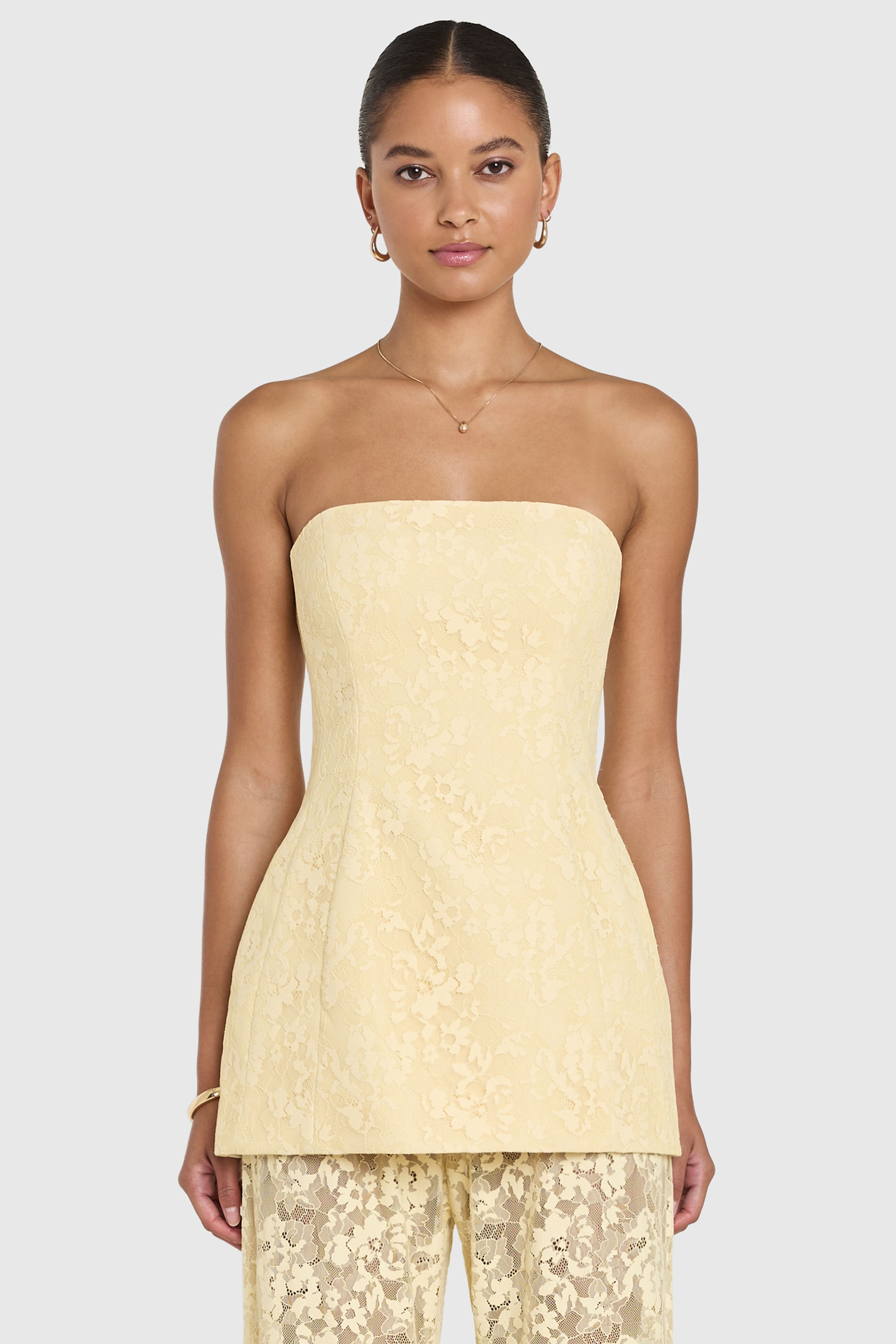 Woman wearing a light yellow strapless top with matching pants on a white background