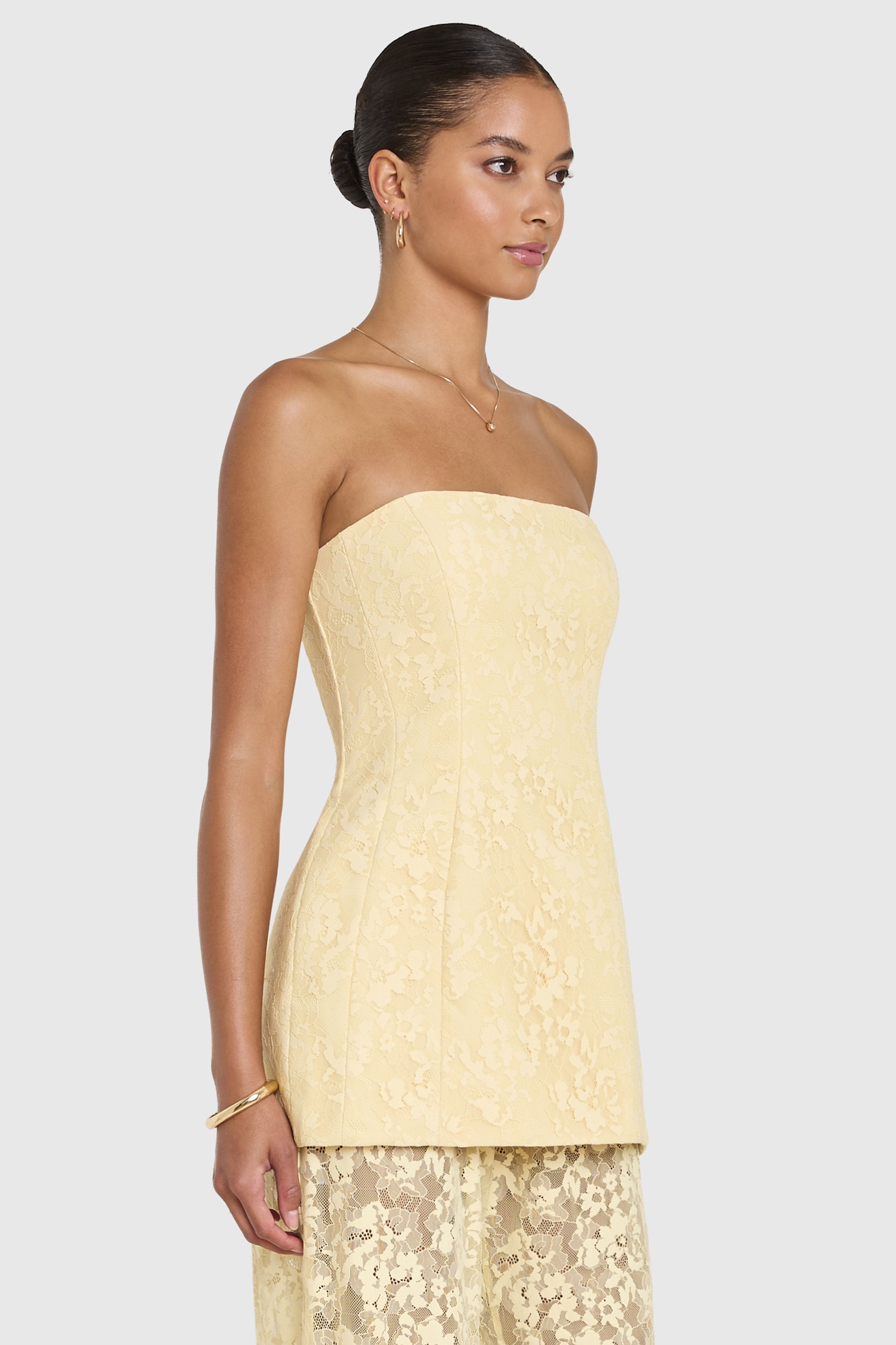 Woman wearing a light yellow strapless dress with lace details on a white background