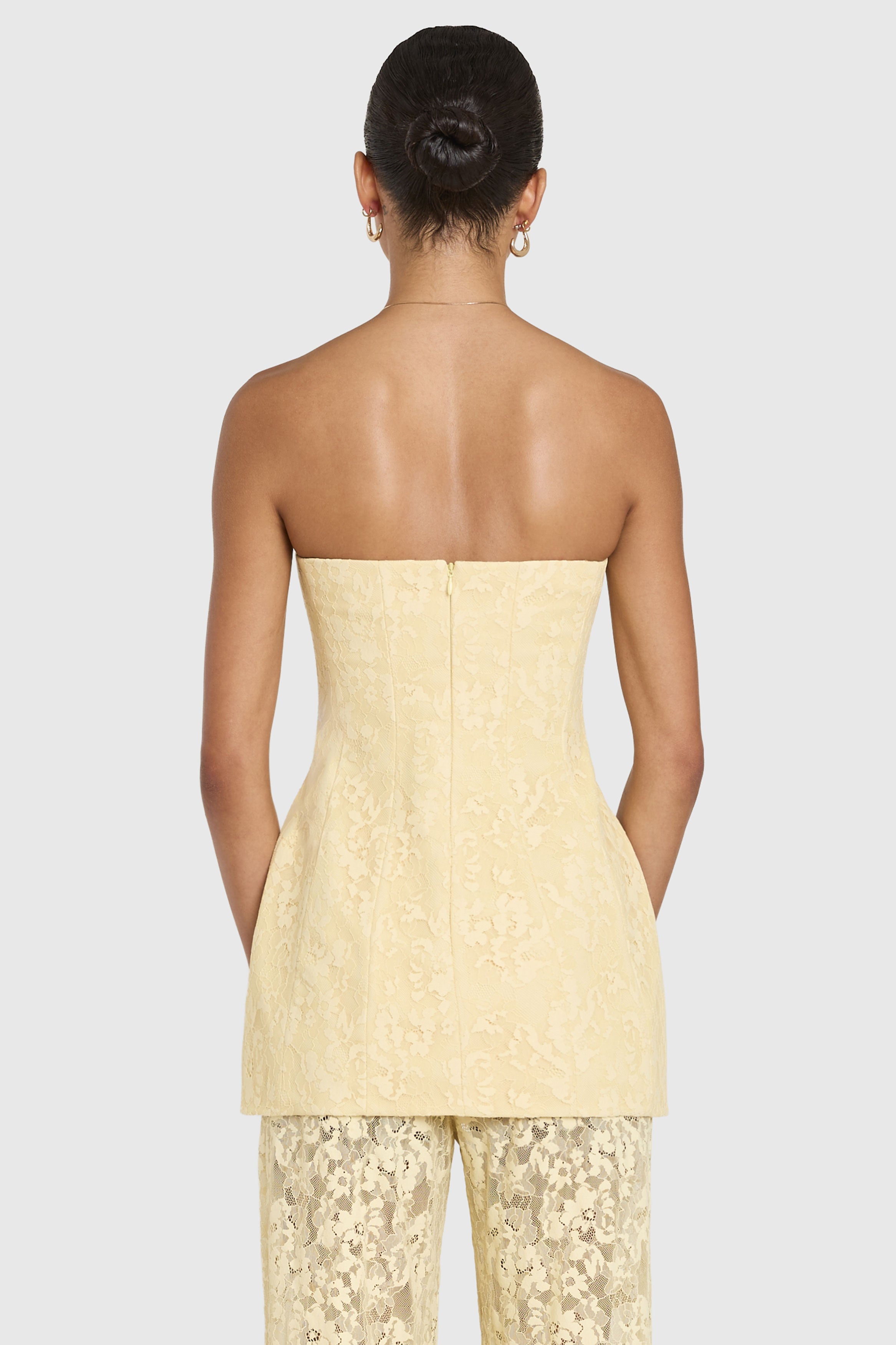 Woman wearing a light yellow strapless top and pants on a white background