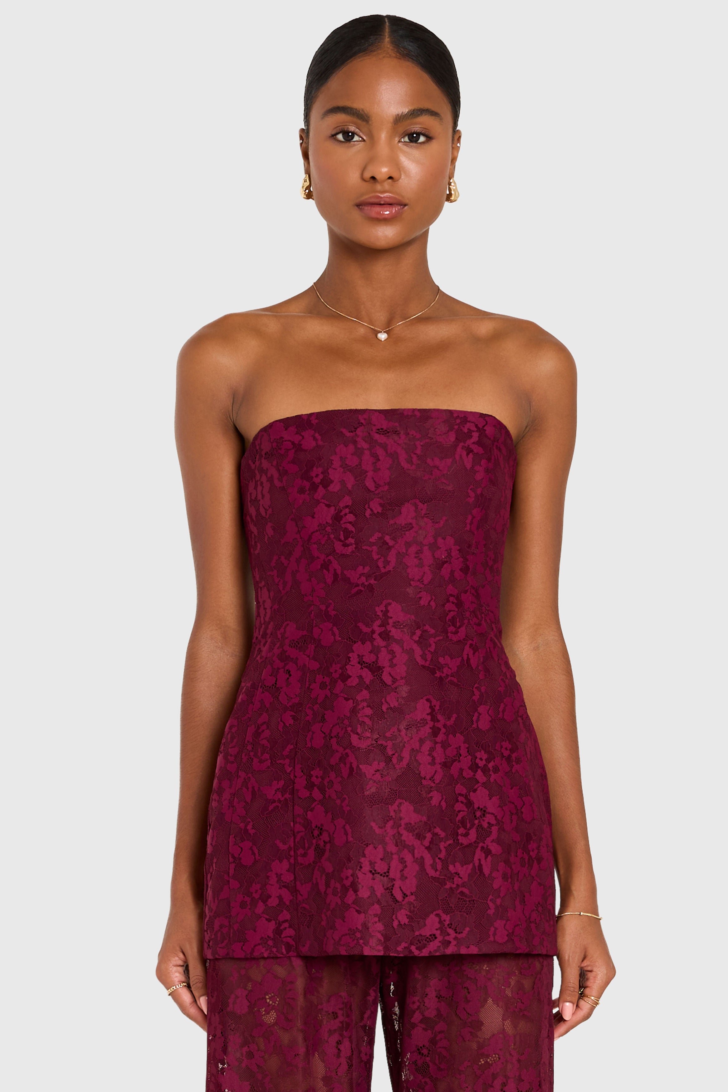 Woman wearing a strapless burgundy lace jumpsuit on a white background