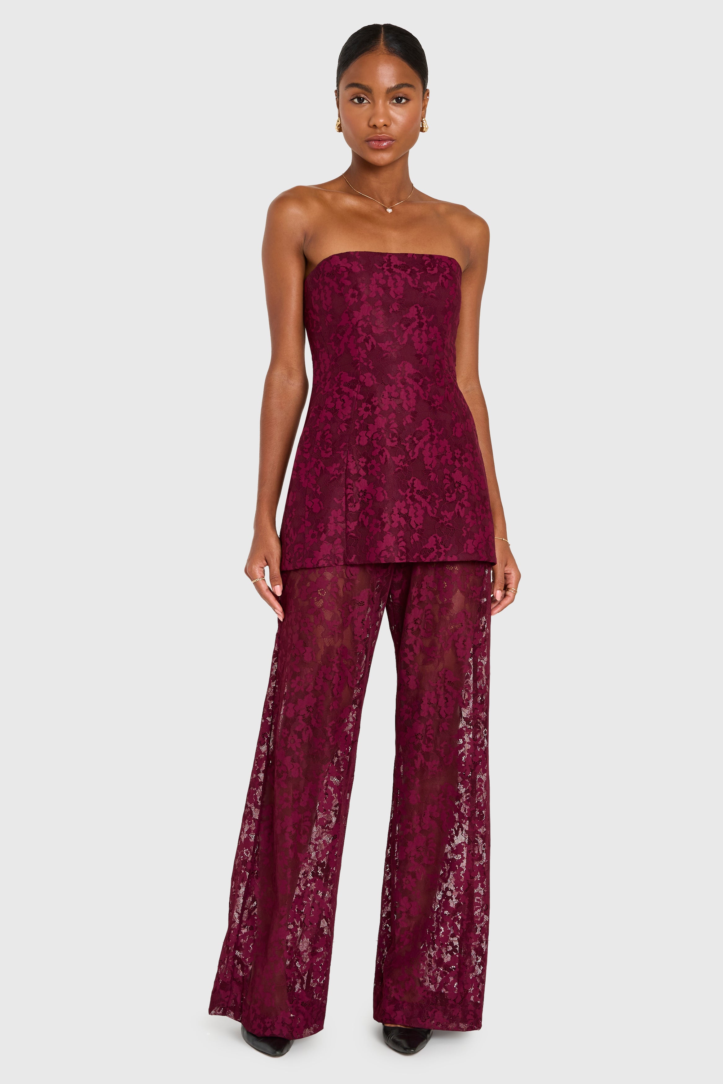 Woman wearing a burgundy strapless top and wide-leg pants on a white background
