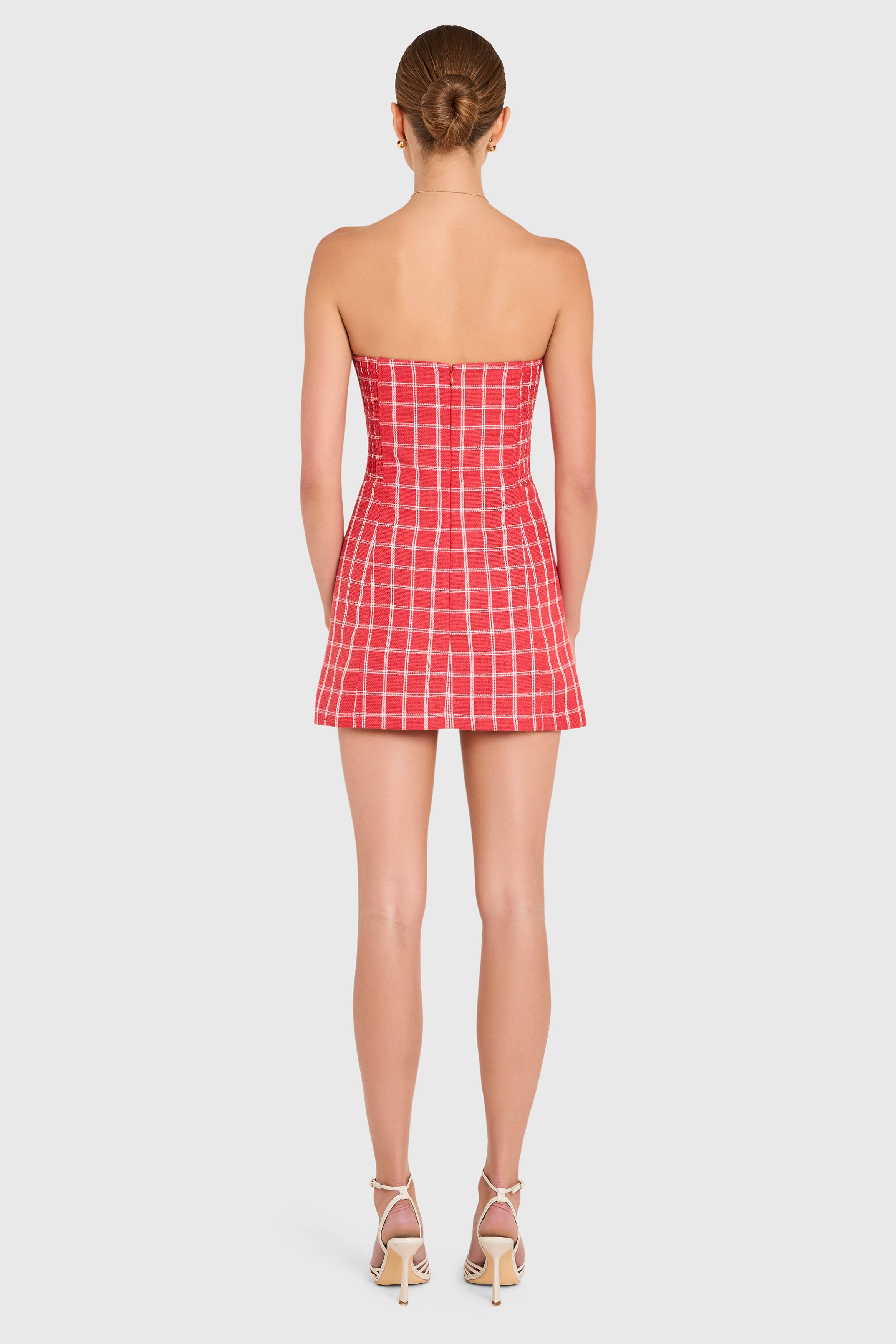 Amanda Uprichard |   Daisy Romper in Mackenzie Plaid. Model wears a red and white plaid strapless mini dress against a white backgorund.