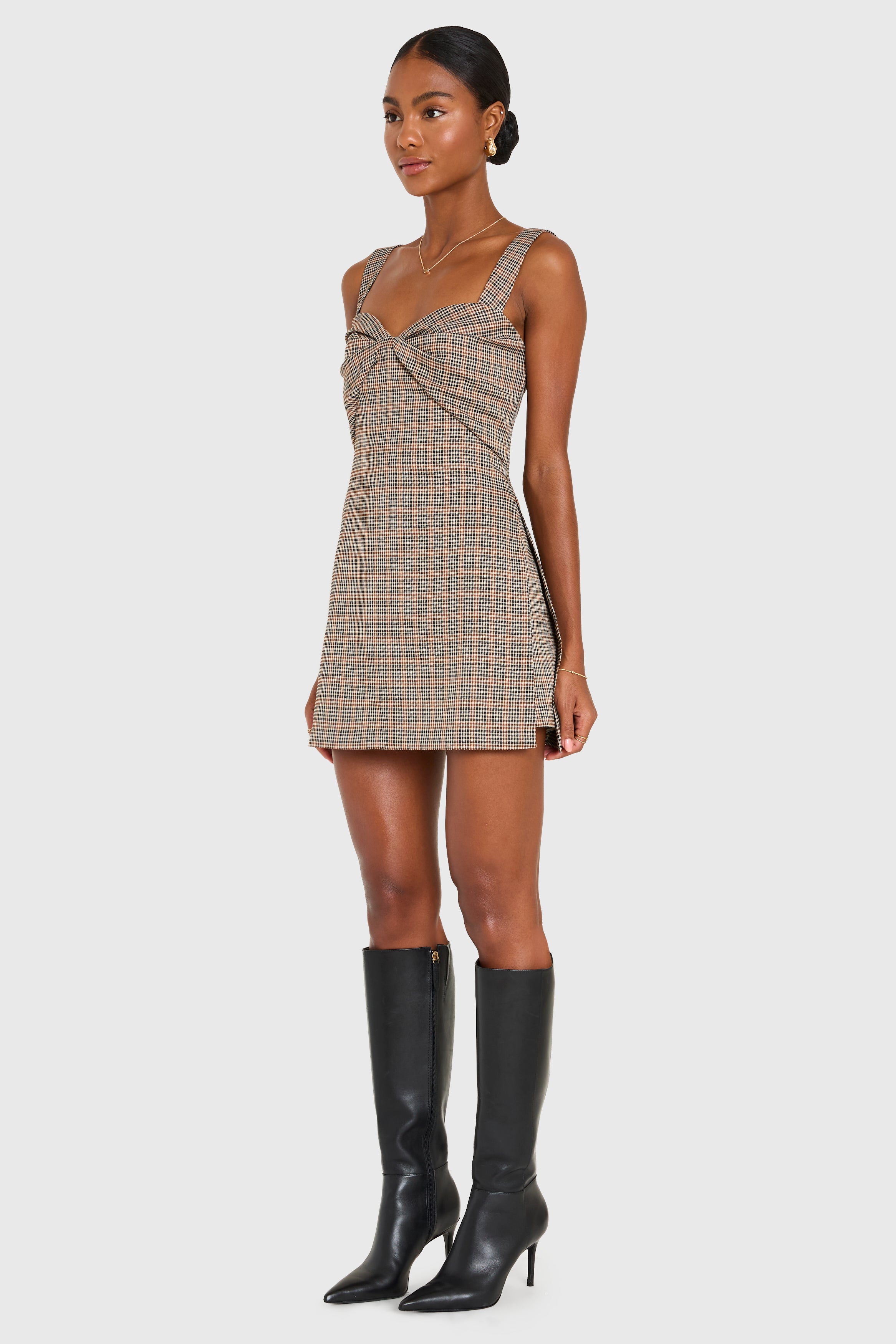 Woman wearing a plaid dress with black knee-high boots on a white background