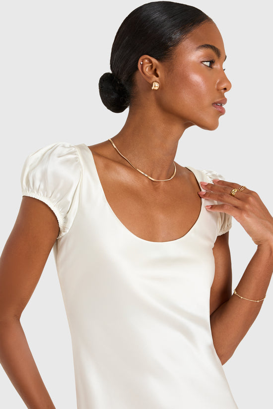 Woman wearing a white satin dress with gold jewelry on a plain background