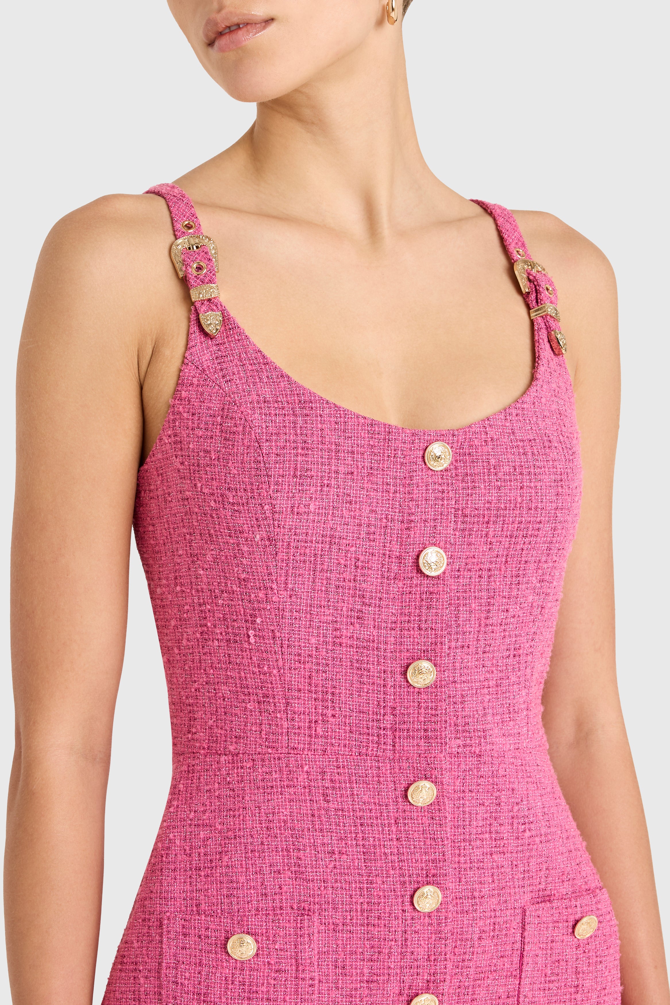 Close-up of a pink textured dress with gold buttons on a white background