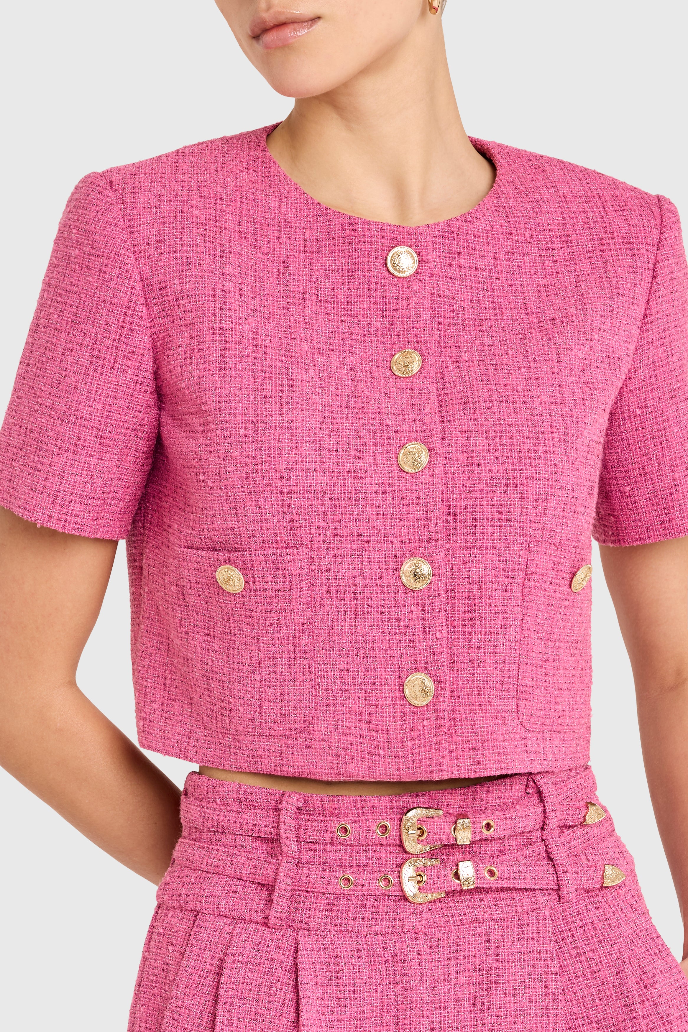 Pink textured outfit with gold buttons on a white background