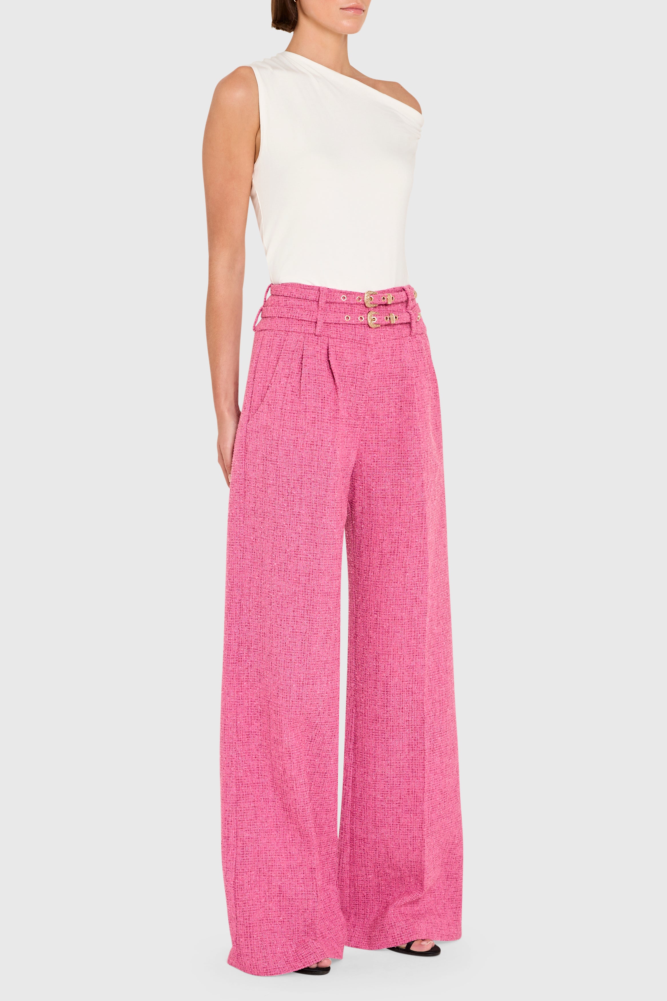 Woman wearing a white sleeveless top and pink wide-leg pants on a white background