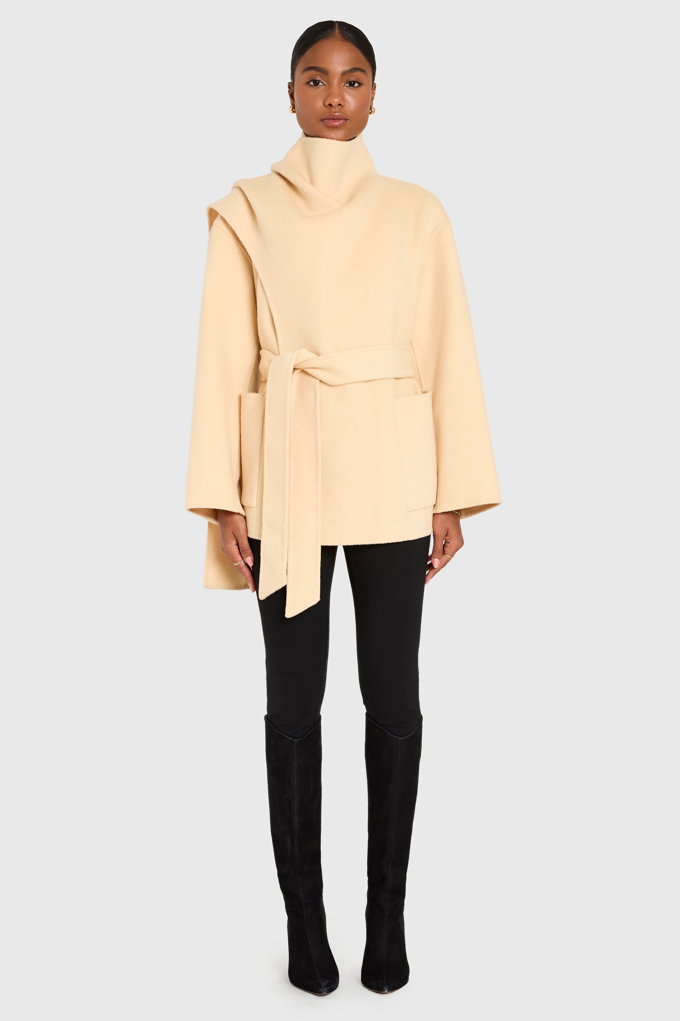 Person wearing a beige coat, black pants, and black boots on a white background
